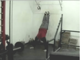 Man Legs on wall doing push ups in a gym.