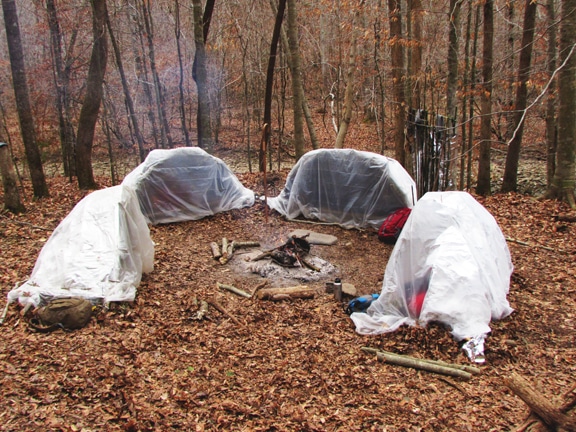 A group of shelter beds around the burning fire in forest.